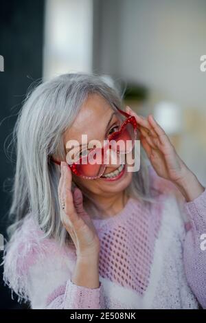 Portrait d'une femme âgée avec des lunettes de soleil à l'intérieur à la maison, en riant. Banque D'Images