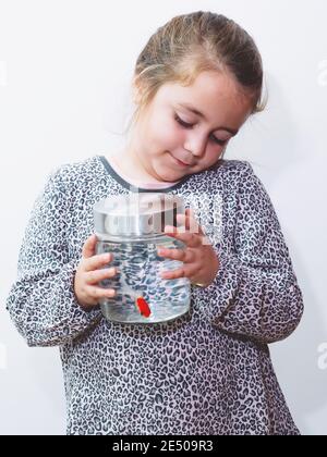 Photo verticale d'une petite fille caucasienne tenant un pot avec un poisson orange à l'intérieur Banque D'Images