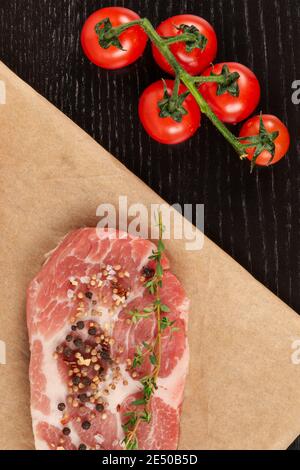 steaks de porc crus fraîchement hachés avec épices et thym sur une feuille de parchemin. tomates rouges mûres Banque D'Images