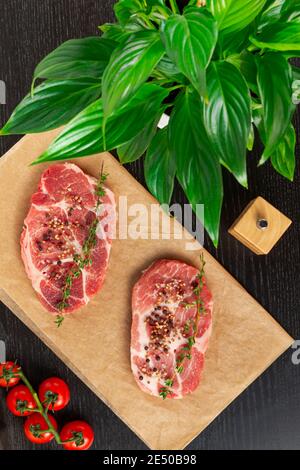steaks de porc frais hachés avec épices et thym sur une feuille de parchemin. à côté de tomates rouges mûres et d'un saupoudreur Banque D'Images