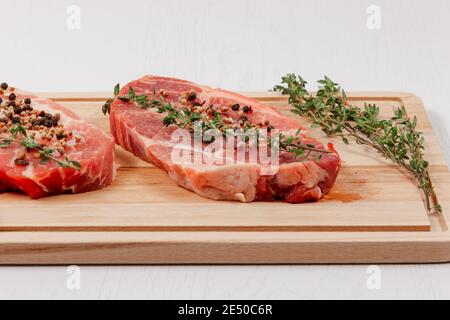 steaks de porc frais, hachés, aux épices et au thym une planche à découper sur une table en bois blanc Banque D'Images