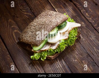 gros plan de sandwich de dinde avec des feuilles de laitue verte, des œufs hachés, des concombres et du pain de seigle ou de blé, sur fond de table rustique foncé en bois, personne Banque D'Images