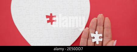 Main de womans tenant la dernière pièce des puzzles en forme de gros plan du cœur Banque D'Images