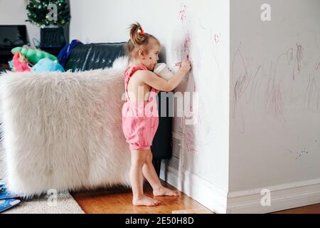 Joli dessin de bébé fille drôle avec un marqueur sur le mur à la maison. Petite fille enfant avec un biberon jouant à la maison. Authentique style de vie d'enfance Banque D'Images