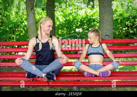 Mère avec fille portant des vêtements de sport assis sur le banc le parc d'été Banque D'Images