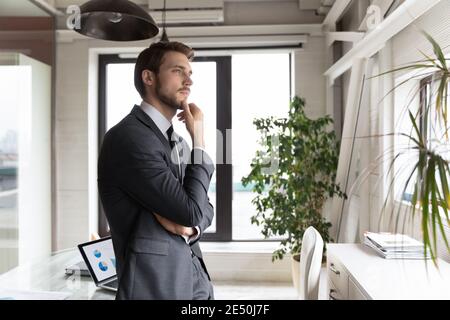 Homme d'affaires attentionné portant un costume touchant le menton, regardant de côté Banque D'Images