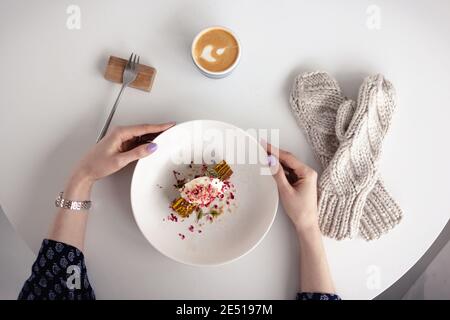 La fille tient une assiette avec un gâteau, à côté des moufles. La vue du dessus. Concept d'hiver, chaleur, vacances, événements. Mise au point douce. Banque D'Images