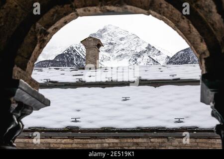 Un toit recouvert de neige avec une cheminée sur le sommet et les sommets lointains de montagne, comme vu de l'arche ronde d'un cloître Banque D'Images