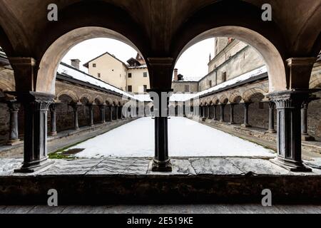 Vue symétrique d'un cloître médiéval en pierre noire du nord de l'Italie, avec des arcs ronds et des colonnes appariées Banque D'Images