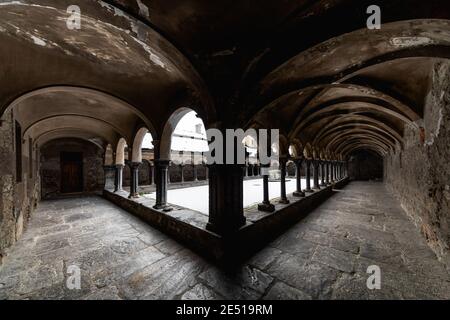 Vue symétrique grand angle d'un cloître médiéval en pierre noire du nord de l'Italie, avec des arcs ronds et des colonnes appariées Banque D'Images