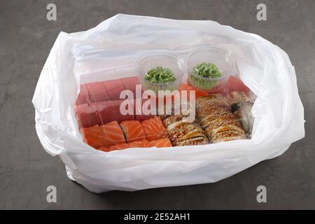 Concept sushi To Go. Boîte à nourriture jetable avec rouleaux à sushi et baguettes dans un sac en plastique sur fond sombre. Sashimi. Saumon. Thon. Anguille. Japonais t Banque D'Images