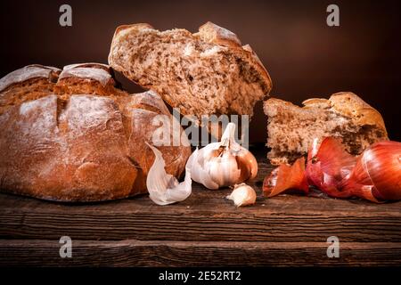 Pain de campagne avec morceaux de miettes, gousses d'ail et échalotes sèches françaises sur un panneau de bois de grange Banque D'Images