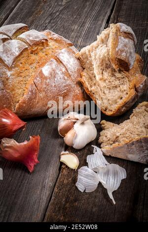 Pain de campagne avec morceaux de miettes, gousses d'ail et échalotes sèches françaises sur un panneau de bois de grange Banque D'Images