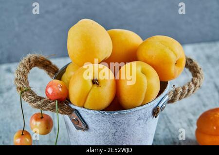 Délicieux abricots mûrs dans un seau en fer avec cerises sur marbre arrière-plan Banque D'Images