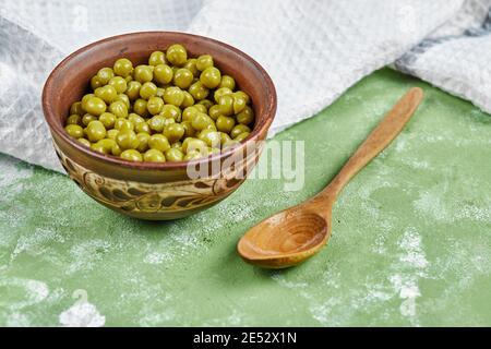 Un bol de pois verts bouillis avec une cuillère en bois et une nappe sur fond vert Banque D'Images