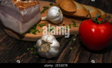 Cuisine maison, cuisine dans la cuisine, bacon avec tomate et ail sur un plateau en bois, aliments frais. Banque D'Images