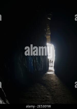 Chiffres flous rétroéclairés de deux personnes marchant dans la lumière des grottes de la cathédrale sur la plage de Waipati dans la région de Catlins sud de la Nouvelle-Zélande. Banque D'Images