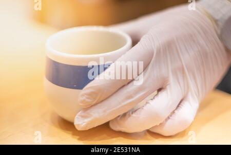 Un serveur portant des gants médicaux tenant une tasse de thé vert de verser le thé dans ses mains. Mesures de protection en raison d'un verrouillage de quarantaine, prendre et aller c Banque D'Images