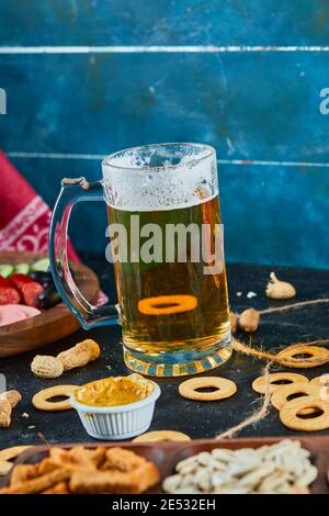 Assortiment de collations, craquelins, une assiette de saucisses et un verre de bière sur fond sombre Banque D'Images
