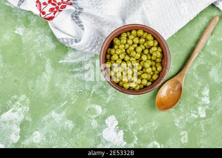 Un bol de pois verts bouillis avec une cuillère en bois et une nappe sur fond vert Banque D'Images