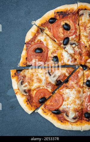 Pizza végétarienne maison aux tomates et aux champignons coupée en tranches un arrière-plan en ardoise Banque D'Images