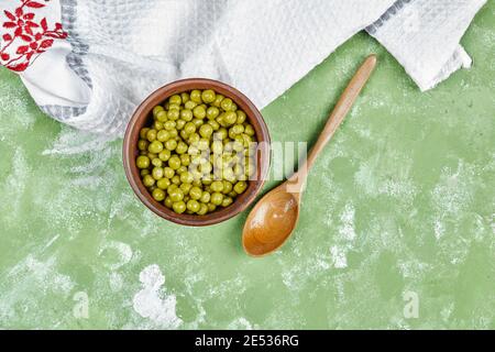 Un bol de pois verts bouillis avec une cuillère en bois et une nappe sur fond vert Banque D'Images