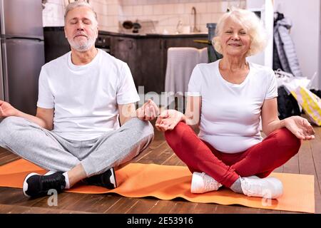 couple mature assis sur le sol méditant dans la posture du lotus, engagé dans le yoga, garder le calme avec les yeux fermés Banque D'Images