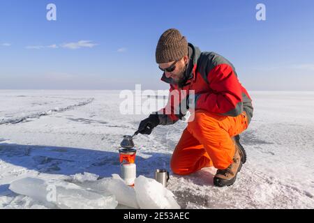 Randonneur avec cuisinière à gaz portable faisant du café sur un champ de glace sans fin recouvert de neige. Randonnée extrême en hiver. Banque D'Images