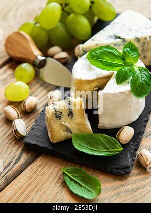 Divers types de fromage, raisins et noix sur une ancienne table en bois Banque D'Images