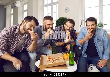 Groupe de jeunes amis affamés regardant un match sportif, buvant de la bière et mangeant de la pizza Banque D'Images