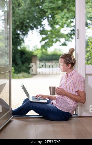 Femme d'affaires travaillant à la maison sur un ordinateur portable pendant une séance de verrouillage en cas de pandémie Dans la porte avant ouverte Banque D'Images
