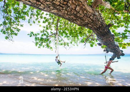 Joyeux garçon et fille jouant sur l'oscillation au bord de la mer un jour d'été. Koh Mook, Thaïlande. Banque D'Images