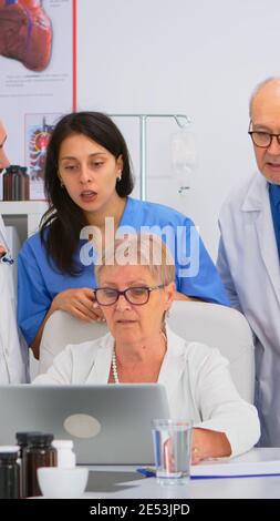 Équipe médicale discutant du diagnostic des problèmes de traitement des patients sur le lieu de travail à l'aide d'un ordinateur portable. Groupe de médecins, travail d'équipe personnes ayant la santé conférence de brainstorming dans la salle de réunion de l'hôpital. Banque D'Images