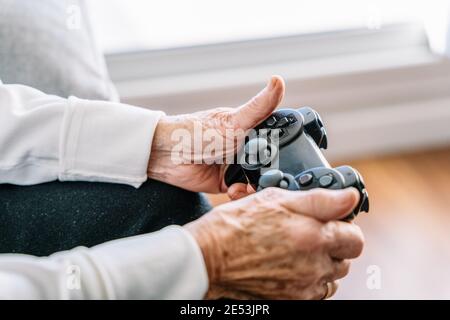 Crop anonyme 90 ans femme assis sur le canapé avec contrôleur moderne et jeux vidéo à la maison Banque D'Images