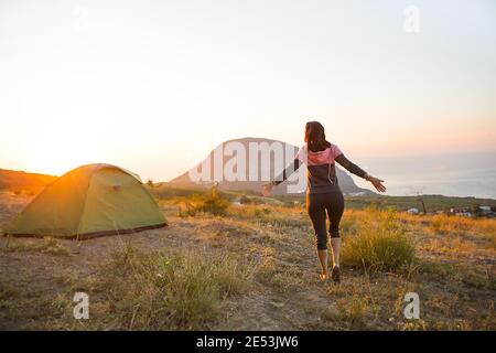 La femme rencontre l'aube dans les montagnes, se réjouit au soleil. Vue panoramique sur la montagne et la mer depuis le dessus. Camping, activités de plein air, sports Banque D'Images