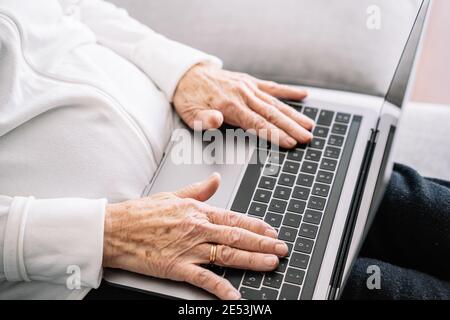 Grande angle de récolte anonyme senior femelle assis sur un canapé et de naviguer sur netbook tout en vous relaxant chez vous le week-end Banque D'Images