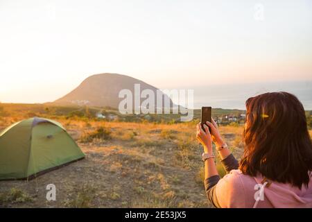 Femme prend des photos du lever du soleil dans les montagnes sur son téléphone. Selfie au soleil levant. Vue panoramique sur la mer et Ayu-Dag. Camping, activités de plein air, Banque D'Images