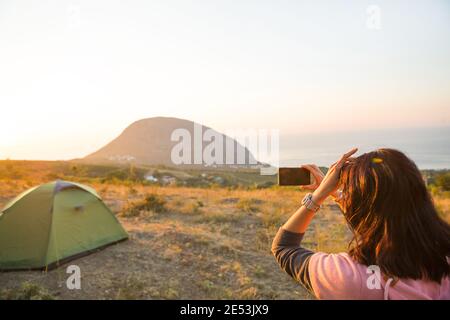 Femme prend des photos du lever du soleil dans les montagnes sur son téléphone. Selfie au soleil levant. Vue panoramique sur la mer et Ayu-Dag. Camping, activités de plein air, Banque D'Images