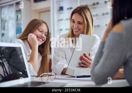 Jolie blonde femme caucasienne avec une jeune femme en affaires décontracté vêtements regardant le presse-papiers dans le centre d'opticien Banque D'Images