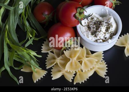 Vue de dessus de Spaghetti et de farfale ingrédients tomates et la maison avec épices sur fond noir Banque D'Images