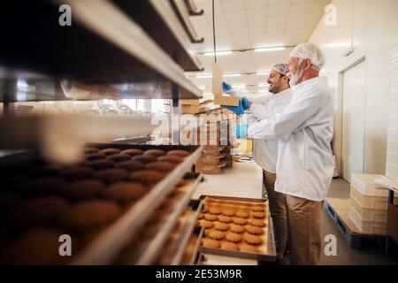 Les travailleurs emballant des biscuits dans des boîtes lorsqu'ils se trouvent dans une usine alimentaire. Banque D'Images