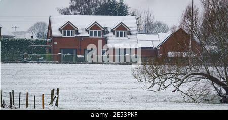 une carte postale d'hiver avec une belle maison en briques rouges et le champ adjacent recouvert d'une couverture de neige Banque D'Images