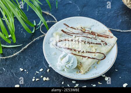 Crêpes à la crème glacée, saupoudrer, chocolat sur la plaque blanche sur fond sombre Banque D'Images