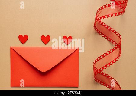 Concept romantique pour la Saint-Valentin ou le mariage. Ruban décoratif torsadé et enveloppe rouge avec coeurs rouges sur fond beige Banque D'Images