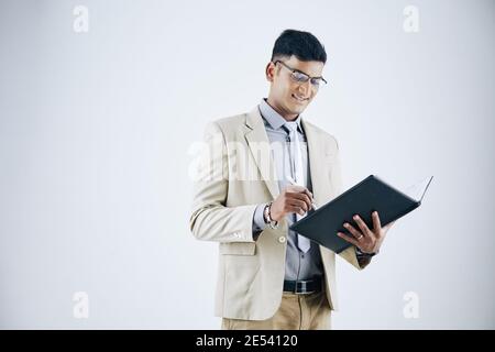 Portrait d'un jeune homme d'affaires indien souriant et réussi qui remplit le document vers le dossier Banque D'Images