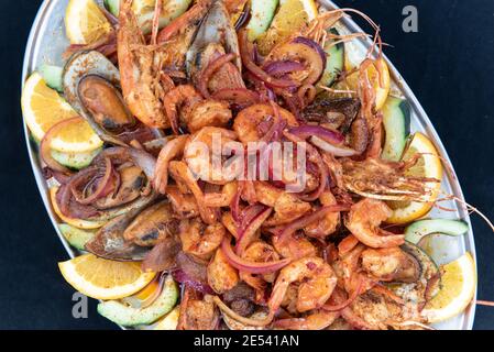 Vue en hauteur d'une grande pile de crevettes épicées servies sur des légumes rôtis et garnies de tranches d'orange. Banque D'Images