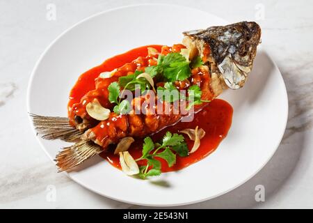 Cuisine chinoise : écureuil de carpe ou songshu yu sous une sauce aigre-douce et de la coriandre fraîche servie sur une assiette blanche sur un fond de pierre de marbre blanc, à Banque D'Images