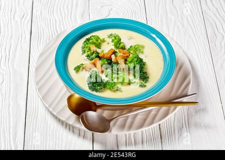 soupe à la crème avec brocoli et croûtons dans un bol bleu sur une table en bois blanc avec des cuillères, vue horizontale d'en haut Banque D'Images