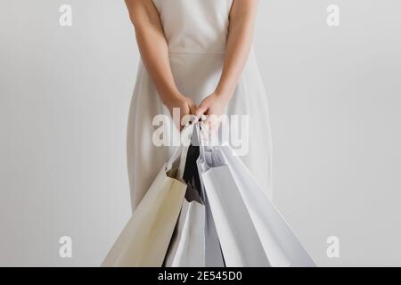 Vue rognée d'une femme en robe blanche tenant des sacs de shopping sur fond blanc. Banque D'Images