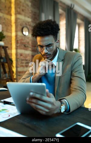 Jeune designer de lunettes assis à la table et en utilisant tablette numérique pour le travail en ligne Banque D'Images